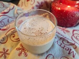 Glass of chilled sugar-free eggnog sprinkled with nutmeg beside a red candle