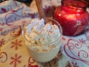 Glass of sugar-free eggnog topped with whipped cream and nutmeg beside a red candle
